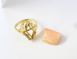 A ladies ring and a rough piece of pink Coral sitting next the ring.
