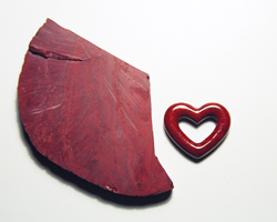 A carved heart shaped red Jasper sitting next to a slab of red Jasper.