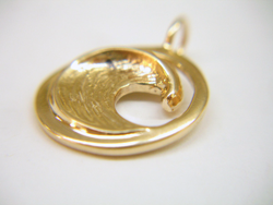 A gold pendant in the round shape of a wave.