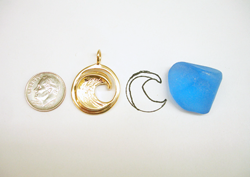 The round gold pendant next to a piece of rough blue topaz which we will use for carving.