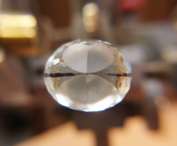 Photo of the bottom of the aquamarine with a black line drawn down the length and 4 facets cut onto the stone.