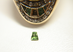 An oval antique ring with green stones. One of the green stones is missing.