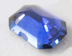 The same emerald cut blue Sapphire face down showing the large chip in the side of the pavilion.