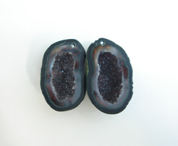 Photo of 2 small geodes which are black and have a small drill hole near the top of each.