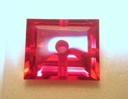 Photo of a red synthetic Ruby with a hole in the center.
