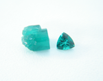 A piece of rough synthetic Emerald next to a trillion synthetic Emerald.