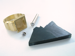 Photo of a ring, a long gold tube with a Diamond, a Masonic emblem, and a piece of rough Black Jade.