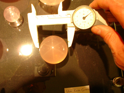 Shows me measuring one of the star rose Quartz spheres with a digital calipers.